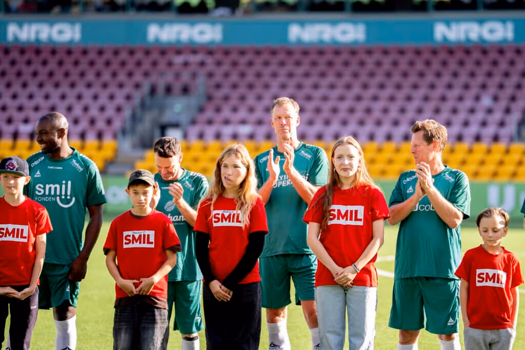 Fodboldspillere med børn i SMIL-trøjer på stadion